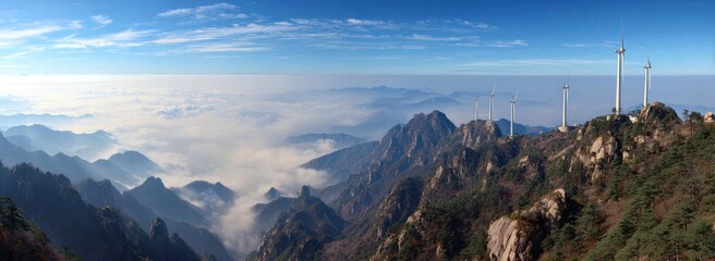Panoramic vista Mountain peaks rise above misty valleys, capped by wind turbines against a blue sky with sparse clouds
