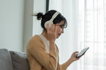 Happy Young Asian woman wearing headphone  listening to music relax in living room
