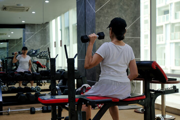 A woman in sportswear and a cap is lifting a dumbbell with her left hand