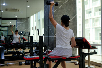 A woman in sportswear and a cap is lifting a dumbbell with her left hand