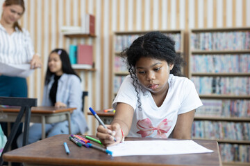 Focused African-American schoolgirl drawing with colored pens at her desk in classroom. Concept of creativity, concentration, childhood education, and individual learning in school setting.