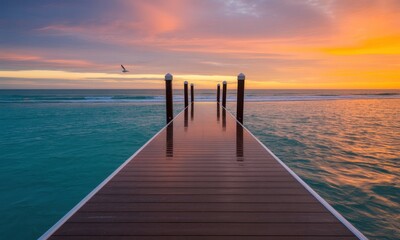 Fototapeta premium Newly constructed dark brown wooden pier extending into turquoise ocean at vibrant sunset with a flying bird