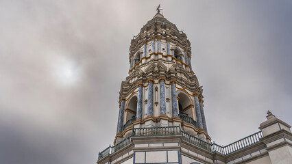 The bell tower of the Catholic Cathedral Basilica and Convent of Santo Domingo against the sky and clouds. A tall tower with columns and arches. Angel statue on top. Peru. Lima. Spanish Colonial  