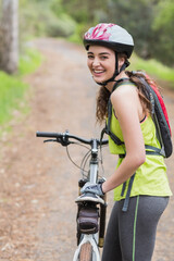 Mountain bike leaning on forest dirt trail, with helmet, gloves, and hydration backpack attached