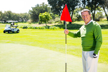 Senior African American man holding red flagstick on putting green with golf cart, copy space