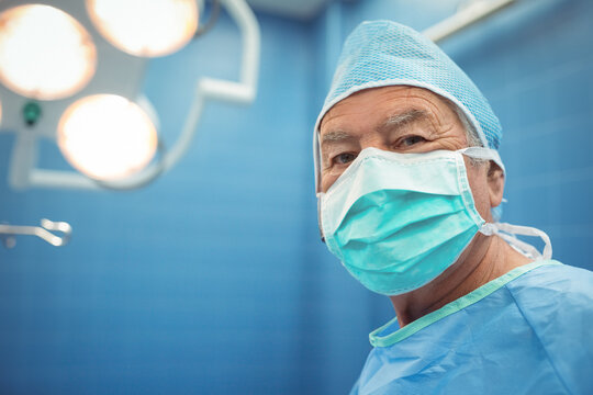 Senior male surgeon standing in operating room wearing cap mask under light near clamp, copy space - Powered by Adobe