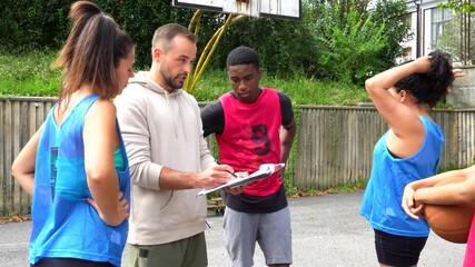 Basketball coach discussing strategy with players on outdoor court - Powered by Adobe