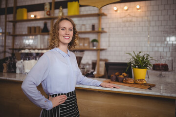 Female barista wearing striped apron serving muffins on board behind countertop at cafe, copy space