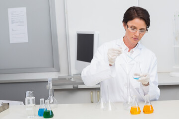Female scientist pouring blue solution from flask into funnel with pipette at lab bench, copy space