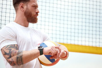 Athlete holding volleyball with net backdrop and focused expression outdoors