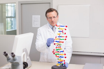 Male scientist wearing gloves and safety glasses examining plastic DNA model in lab with microscope