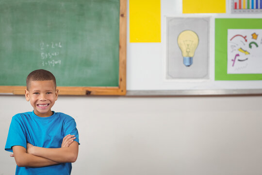 Boy is standing and smiling in front of green chalkboard with math equations and posters