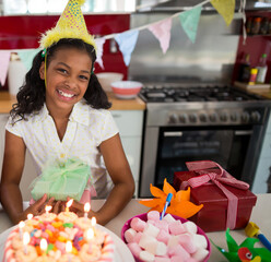 Frosted birthday cake sitting on countertop beneath pastel flags, with bowl of pink marshmallows
