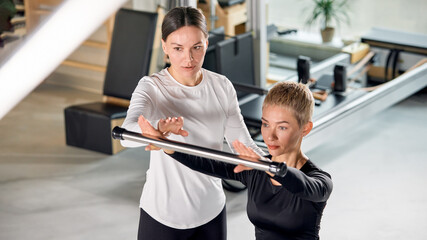 Fitness instructor guiding client in a pilates class at a modern studio