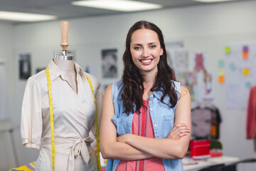 Female designer standing in fashion studio by wrap dress on mannequin with yellow measuring tape
