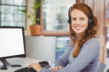Female office worker wearing headset using keyboard and mouse at desk near window with monitor