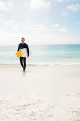 Wetsuit-clad man holding surfboard yellow tip emerging from turquoise water onto beach, copy space