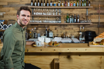 Man sitting at bar counter at cafe drinking coffee with sandwich plate and stirrers, copy space