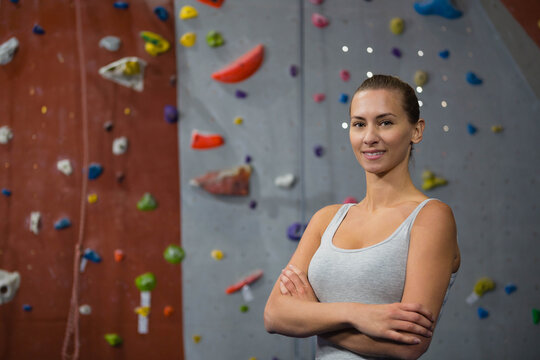 Female climber wearing tank top crossing arms at climbing wall with holds and rope, copy space