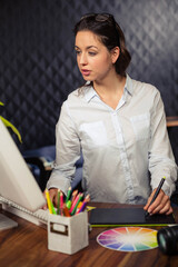 Woman working at wooden desk in design studio using stylus on graphics tablet with color wheel