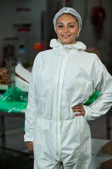 Female operator standing at table in packaging room wearing white protective coverall and hairnet