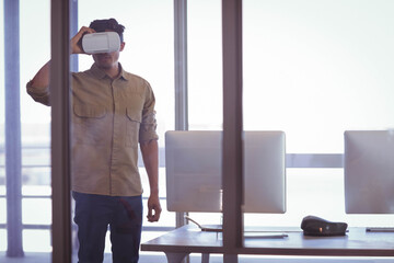 Man wearing VR headset interacting near glass partition in modern office with dual monitors