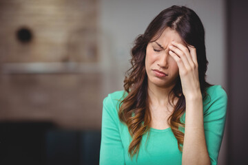 Woman pressing hand against temple while sitting in living room wearing green top, copy space