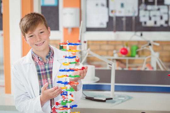 Smiling boy holding plastic DNA double helix model at lab bench wearing lab coat, copy space