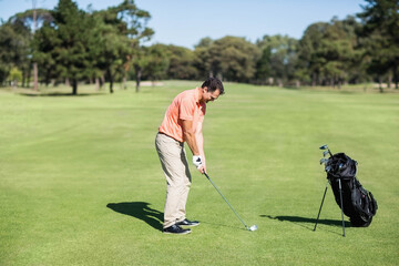 Adult male golfer standing on green fairway, gripping club and aiming at ball with stand bag