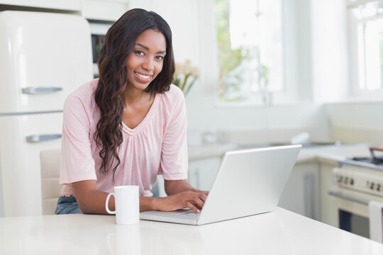 African American woman typing on silver laptop at white kitchen island near ceramic mug and flowers