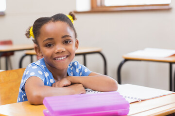 African American girl in blue shirt smiling, resting on notebook with pencil case at school desk