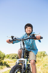 Naklejka premium Boy wearing helmet and blue shirt riding mountain bike on grassy dirt trail among green shrubs