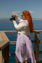 Redhead woman in profile taking photos of the blue sea on a sunny day, concept of travel, vacation,...