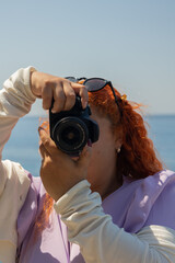 Portrait of redhead woman taking photos of the blue sea on a sunny day, concept of travel,...