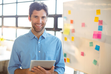 Middle-aged man standing by whiteboard with sticky notes at office using tablet during planning