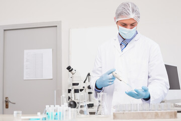 Adjustable pipette dispensing blue liquid into test tube rack on laboratory bench with glassware