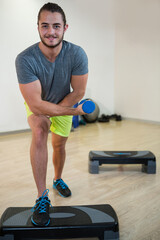 Male exerciser in sportswear performing lunge curl on platform in fitness studio with blue dumbbell