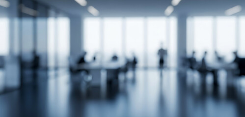 Blurred office interior with people working at desks and large windows, creating a productive atmosphere filled with daylight, collaboration, and modern corporate energy.