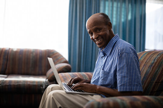 Senior African American man sitting on patterned sofa in living room using laptop, copy space