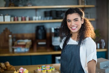 Smiling African American woman serving cupcakes behind counter in café wearing apron, copy space