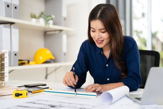 Young female engineer designer or contractor working on drawing plans and making measurements on blueprints of post tension slab plan by triangular scale at workplace, copy space