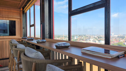 A cafe with chairs and tables against a backdrop showing a bird's-eye view of the city. The cafe is located inside the Ampera Bridge tower in Palembang