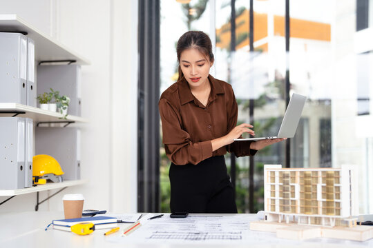 Young female engineer designer or contractor working on drawing plans analyzing structure on laptop computor at construction site office. copy space. - Powered by Adobe