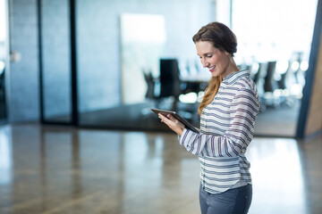 Professional woman standing in office lobby holding tablet in striped top and trousers, copy space