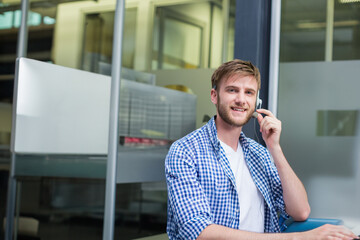 Call center agent wearing headset and checkered shirt smiling and typing at desk by glass partition