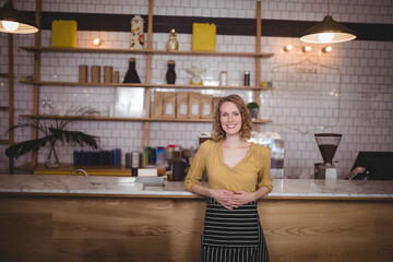 Woman barista wearing mustard blouse and apron operating espresso machine and POS terminal at café