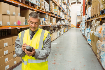 Senior male wearing safety vest scanning boxes with handheld scanner on shelves in warehouse aisle