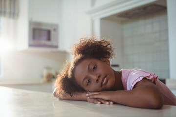 Schoolgirl resting head on countertop as morning sunlight streaming through window near microwave
