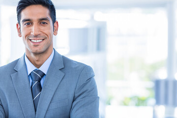 Man standing with crossed arms in bright modern office workspace, wearing grey suit and striped tie