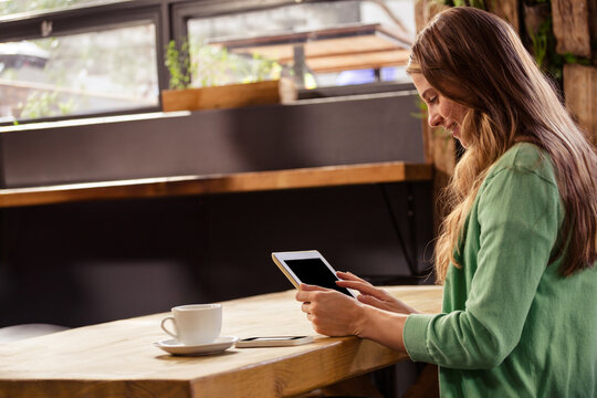 Tablet displaying content and resting on wooden counter beside smartphone and coffee cup in café